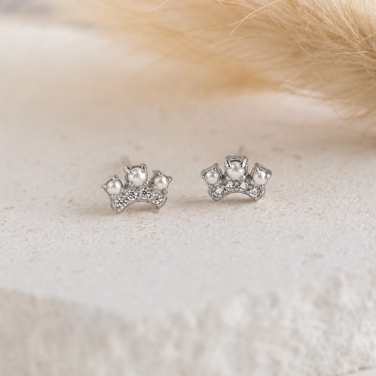 Silver crown-shaped earrings with pearls on a soft beige background